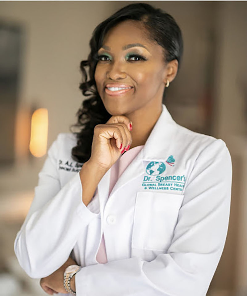 A professional portrait of Dr. April Spencer, a smiling African American woman in a white lab coat, representing her role as a breast health expert and founder of the Global Breast Health & Wellness Center.