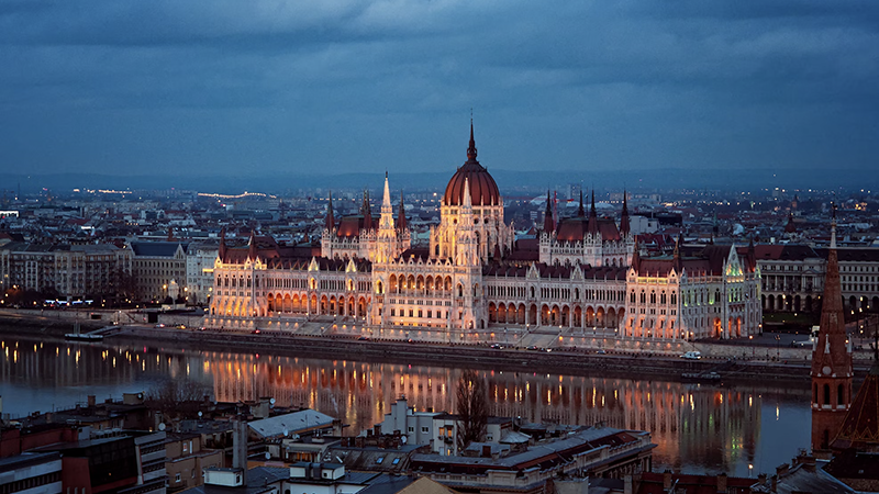 A stunning view of Budapest’s Parliament Building illuminated at night, reflecting on the Danube River, showcasing the city’s charm and affordability.