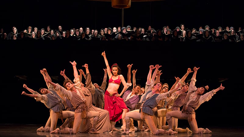 A vibrant theatrical performance featuring dancers in colorful costumes and a chorus in dark robes, captured during Carmina Burana.