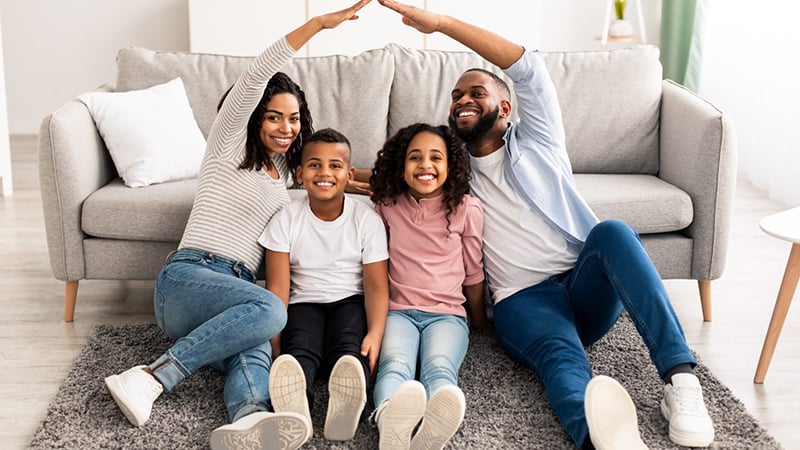 A happy family sitting on a rug in their living room, symbolizing the security and protection offered by homeowners insurance.