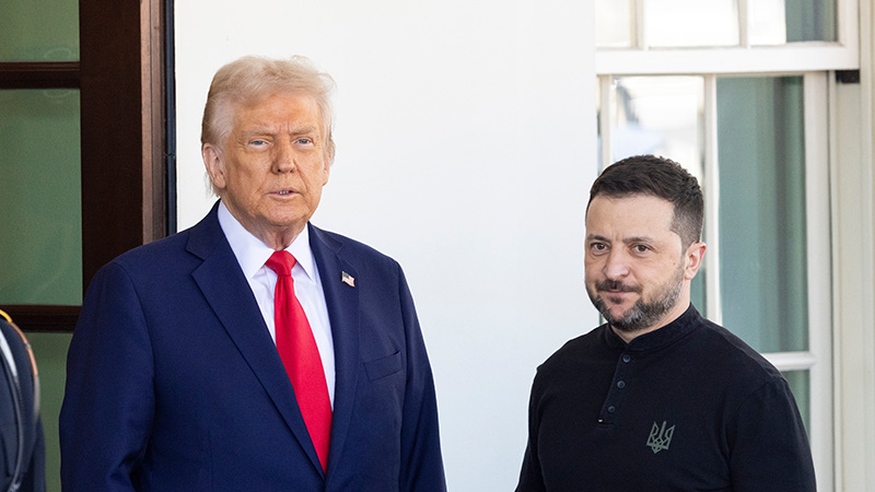 Donald Trump and Volodymyr Zelenskyy standing side-by-side during a formal meeting, with light architecture in the background.