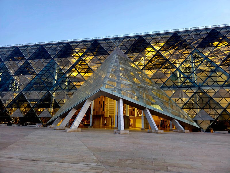 The Grand Egyptian Museum's modern glass facade and pyramid entrance at dusk, glowing with golden light.