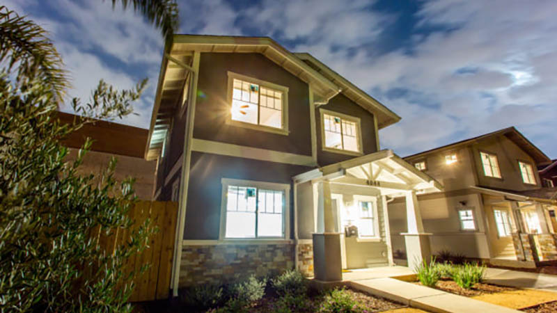 A modern two-story house with warm interior lights, surrounded by greenery, captured at dusk with a clear sky in the background.