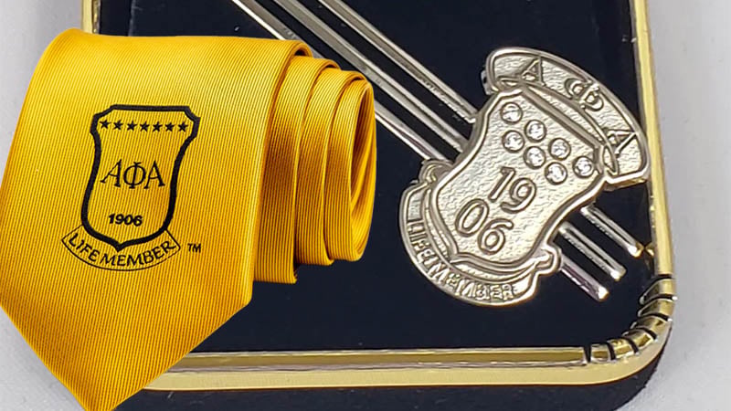 A close-up of the Alpha Silver 1906 Life Member Tie Bar, showcasing its polished silver finish and intricate design on a formal suit.