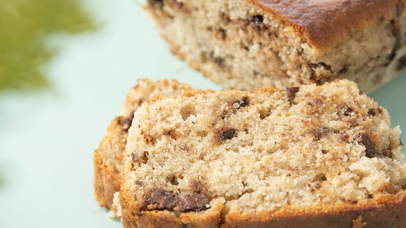 A close-up of moist banana bread slices with chocolate chips, resting on a light green surface, showcasing their rich texture and golden crust.