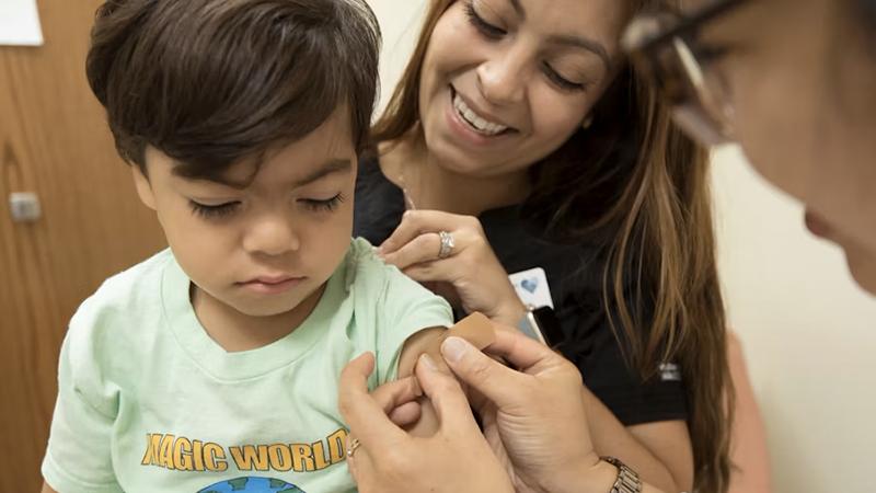 A young child receiving a vaccine, with a parent and healthcare provider offering comfort and care, symbolizing equitable immunization access.