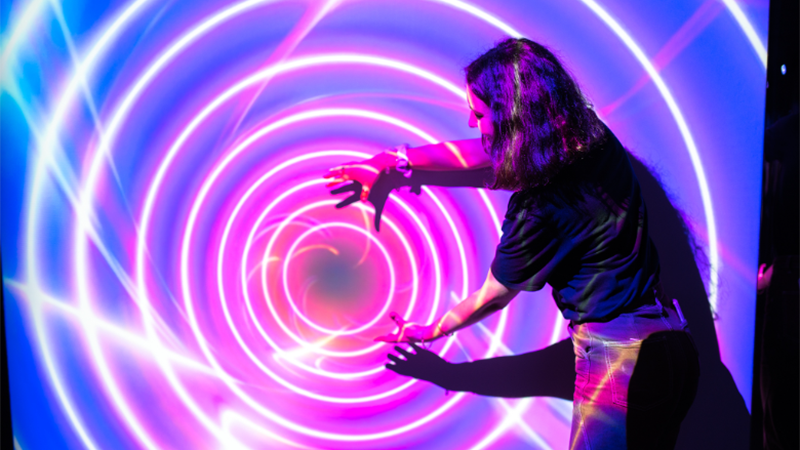 A vibrant scene from Dopamine Land, showcasing glowing concentric rings and a person interacting with the immersive light display.