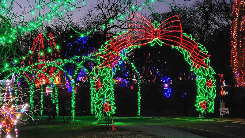 A vibrant nighttime display of holiday lights at the Missouri Botanical Garden, featuring a glowing Christmas tree and illuminated dome.