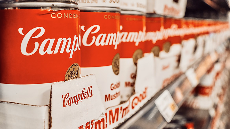A display of Campbell's soup cans with the iconic red and white label, symbolizing the brand's legacy amidst controversy.