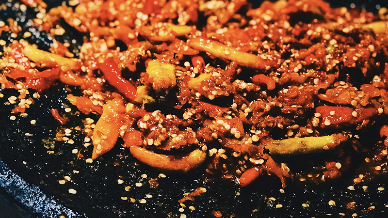 A vibrant dish featuring glossy chili crisps, sesame seeds, and tangy sauce, showcasing the Swicy & Sour food trend of 2026.