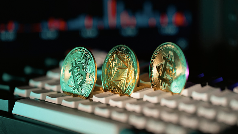 Three cryptocurrency coins, including Bitcoin and Ethereum Classic, standing on a keyboard with a blurred digital chart background.