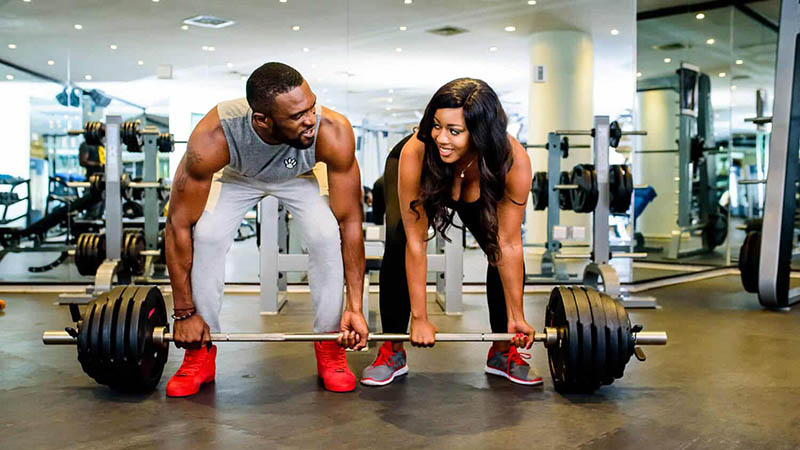 Two individuals performing a deadlift in a gym, symbolizing teamwork and fitness goals.