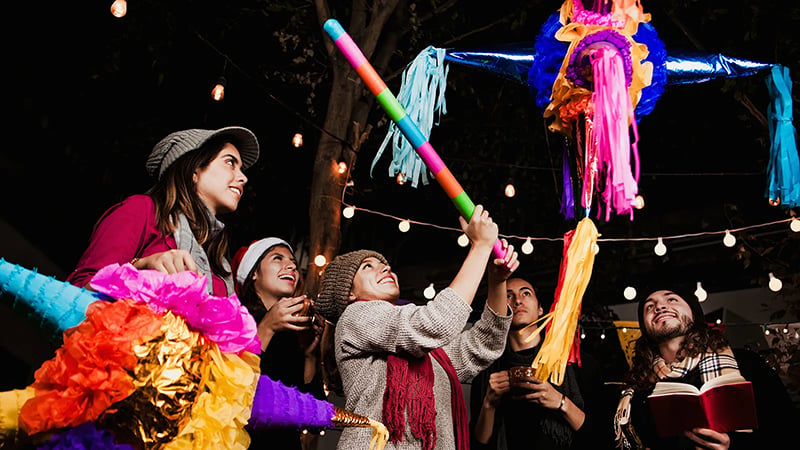 A festive Las Posadas celebration in St. Louis with friends breaking a colorful piñata under string lights, showcasing Latino Christmas traditions.