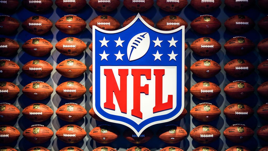A large NFL logo centered on a dark blue background with a grid of brown footballs, each featuring team logos and text, creating a celebratory display of American football."