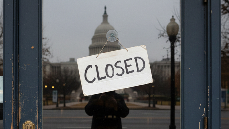 A 'Closed' sign on a restaurant door in Washington D.C., symbolizing economic challenges and reflecting the cityscape.