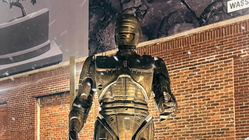 RoboCop statue in Eastern Market, Detroit, with a brick wall backdrop and snow-like specks creating a dramatic atmosphere.
