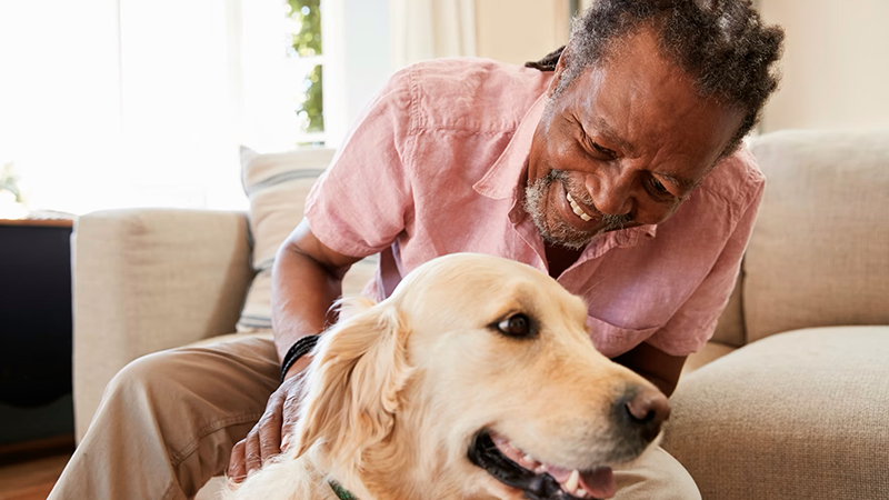 An older Black man smiling warmly at his golden retriever, symbolizing the joy and comfort of self-care and companionship.