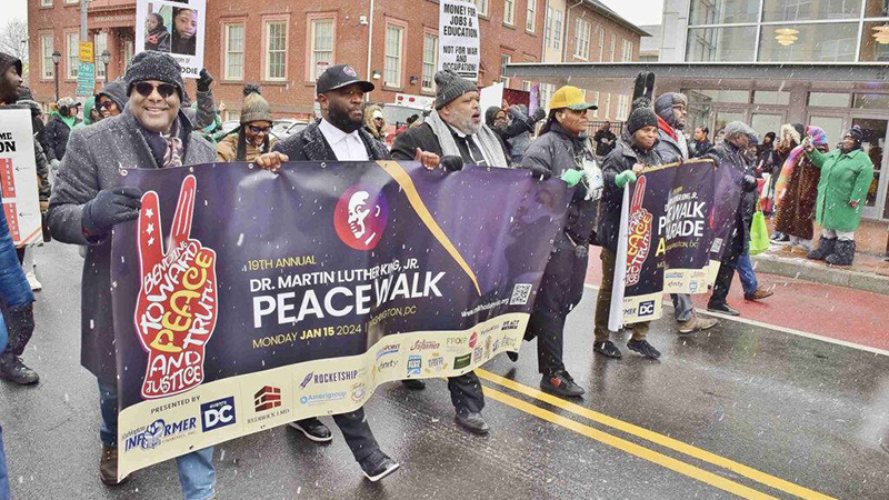 A diverse group of participants walking in the DC MLK Peace Walk, holding banners with messages of peace and justice.