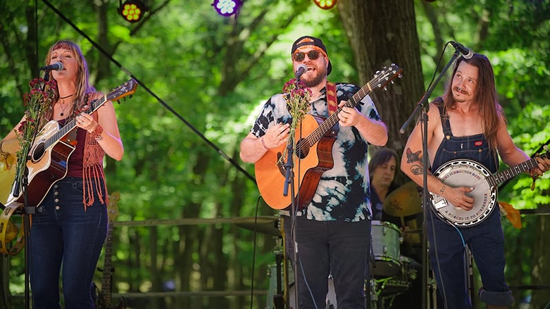 Maygen & The Birdwatcher performing outdoors with acoustic instruments.