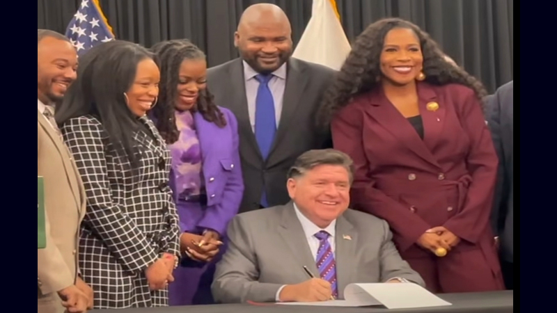 Governor Pritzker signing the Clean Slate law surrounded by diverse supporters.