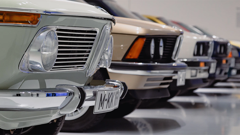 Lineup of vintage cars at the Detroit Auto Show, featuring a mint-green car in the foreground with chrome accents.