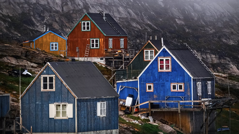 Colorful wooden houses on a rocky Greenland hillside under an overcast sky.