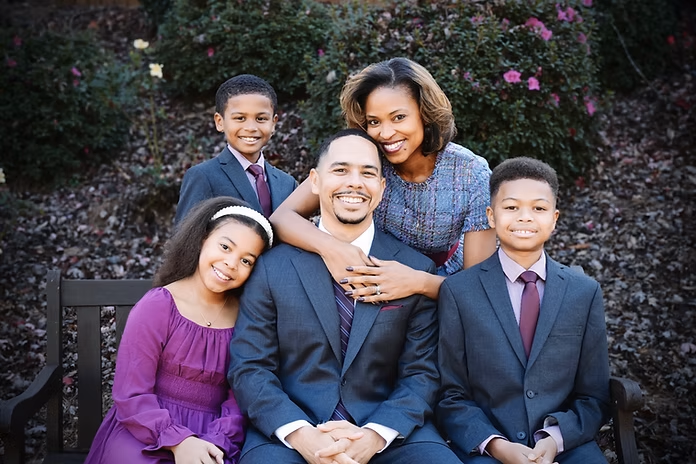 Dr. Jaha Howard posing outdoors with his wife and three children, all smiling and dressed in formal attire.