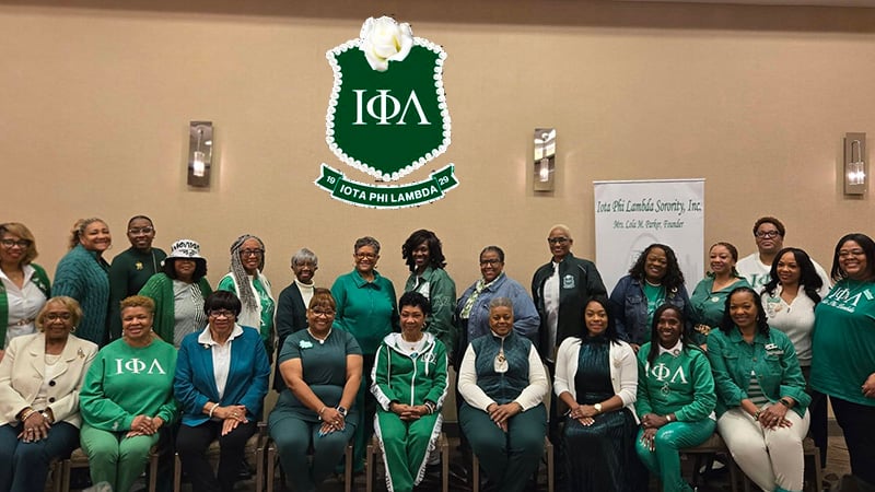 Group photo of Iota Phi Lambda members in green and white attire, showcasing the first African American business sorority's emblem and banner.