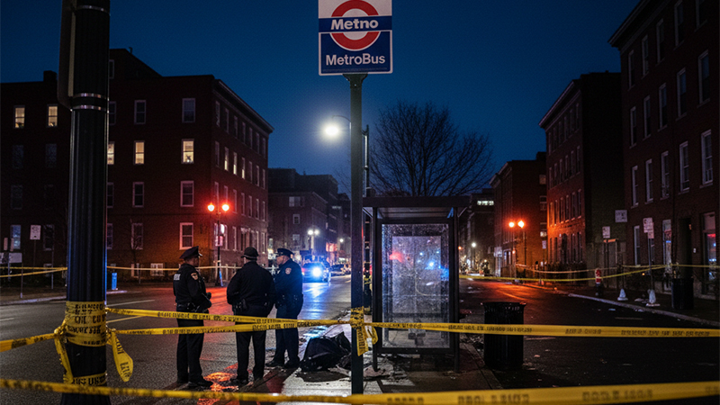 Police tape and emergency lights at a Metrobus stop in Northwest Washington D.C., highlighting a crime scene at night.