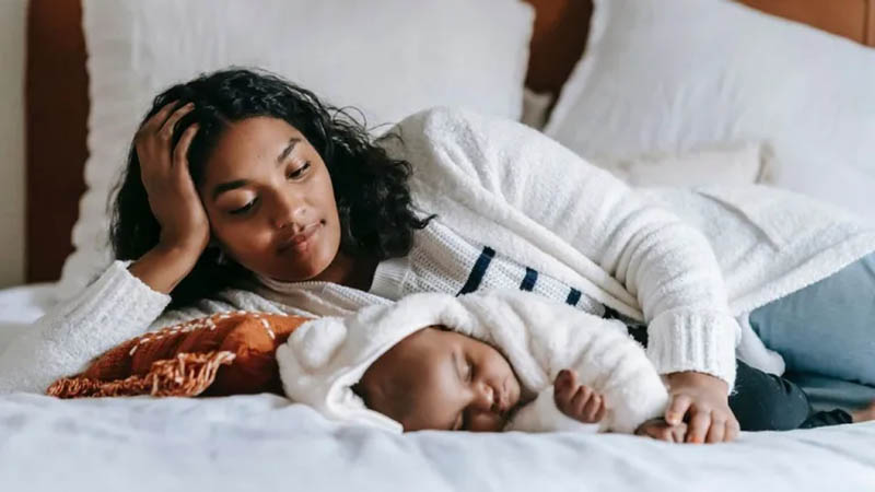 A mother lying next to her sleeping baby, symbolizing the challenges of sleep deprivation in new motherhood.