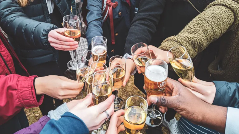 A group of diverse young adults toasting with drinks, symbolizing social gatherings and alcohol consumption.