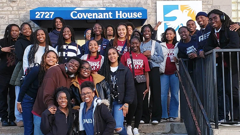 Group of young adults smiling in front of Covenant House Missouri building with a blue awning and logo.