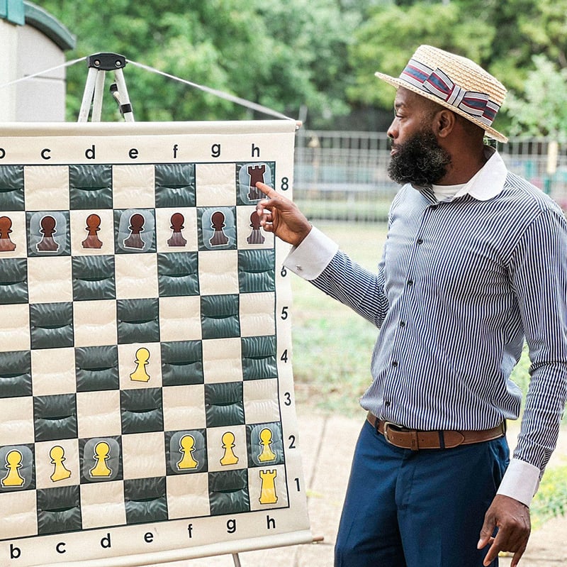 Eric Payne, a chess instructor in St. Louis, smiles while seated at a chessboard ready to teach a lesson on strategic thinking.