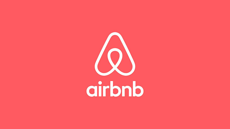 Airbnb logo featuring the Bélo symbol and wordmark in white, centered on a vibrant coral-red background.