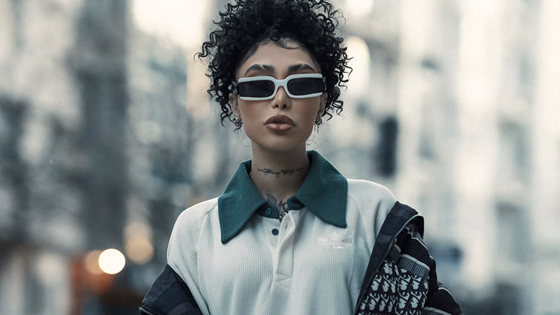 A fashion-forward individual wearing white-framed sunglasses and a mix of sporty and luxury streetwear.