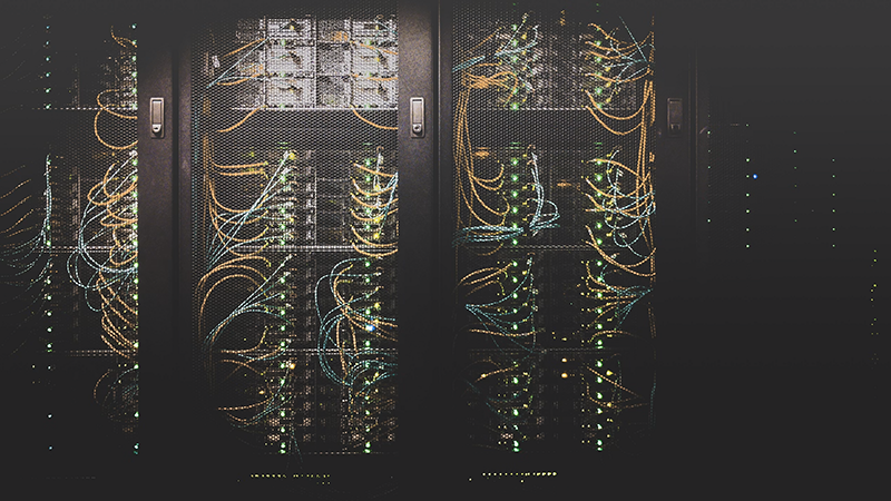 Interior of a data center with server racks, intricate wiring, and glowing green LED lights, symbolizing modern technology and data infrastructure.
