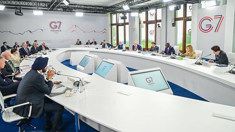 G7 leaders seated at a large, modern round table for a summit meeting in France.
