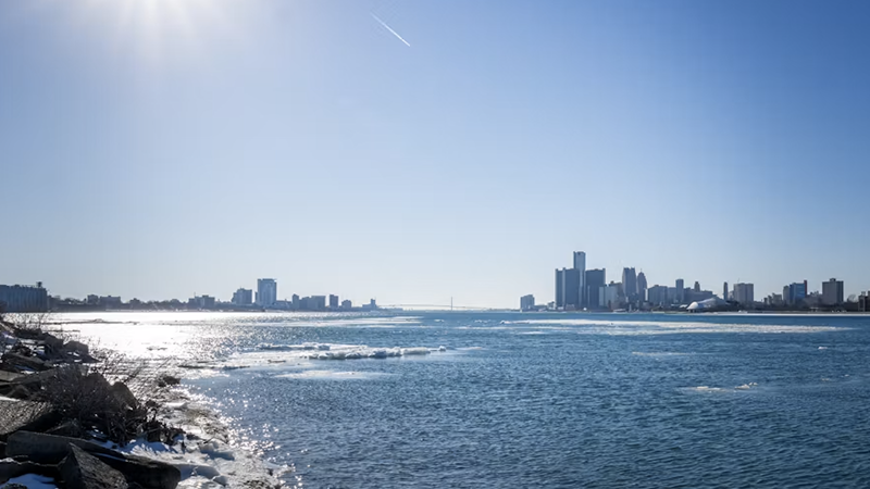 Panoramic view of a city skyline across a partially frozen river under a bright winter sky, symbolizing Metro Detroit's severe weather alert.