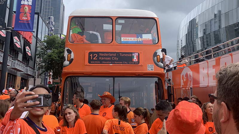 A massive crowd of Dutch soccer fans wearing bright orange shirts gathered around a large orange double-decker fan bus during the World Cup celebration in Kansas City.