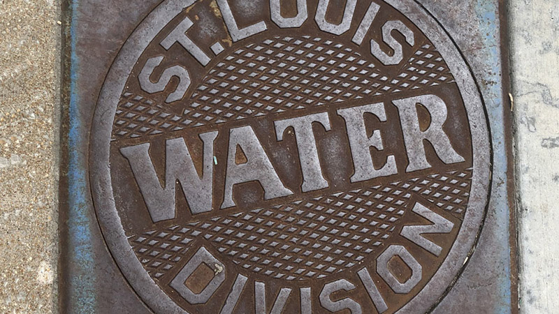 A rusty utility cover labeled “St. Louis Water Division,” symbolizing the city’s water infrastructure and assistance programs.