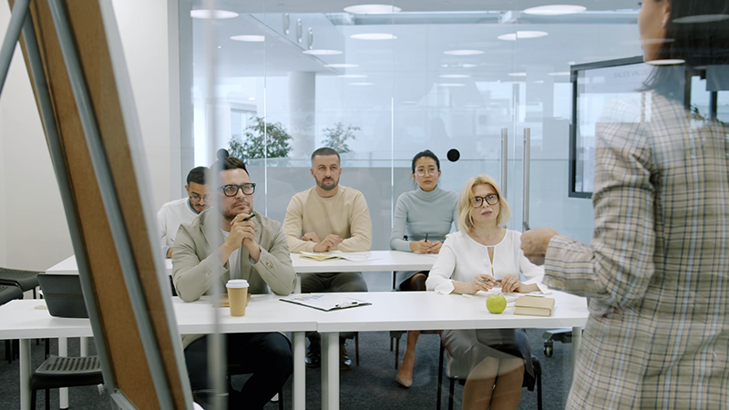 A group of professionals attentively listening to a speaker in a modern conference room, symbolizing workplace collaboration and learning.