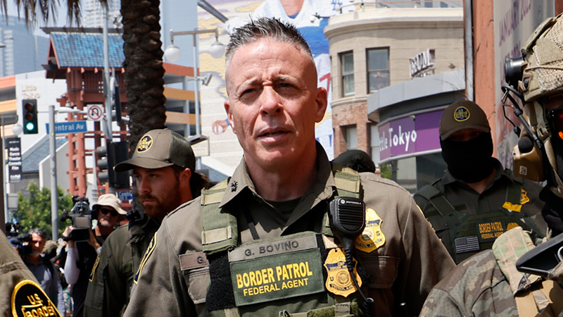 Border Patrol agents in tactical gear during a protest in Chicago's Little Village neighborhood, with urban scenery in the background.