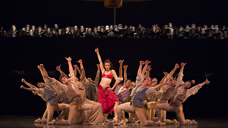 A vibrant theatrical performance featuring dancers in colorful costumes and a chorus in dark robes, captured during Carmina Burana.