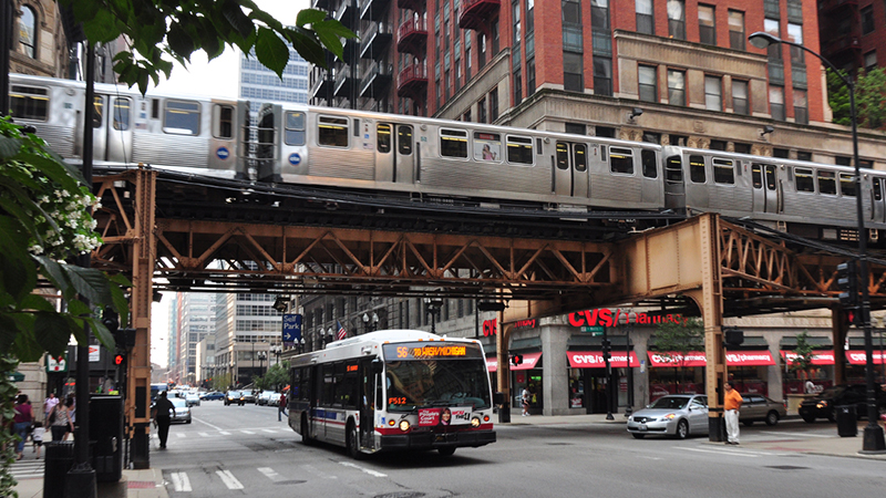 Elevated train and city bus in Chicago, with pedestrians and urban architecture in the background.