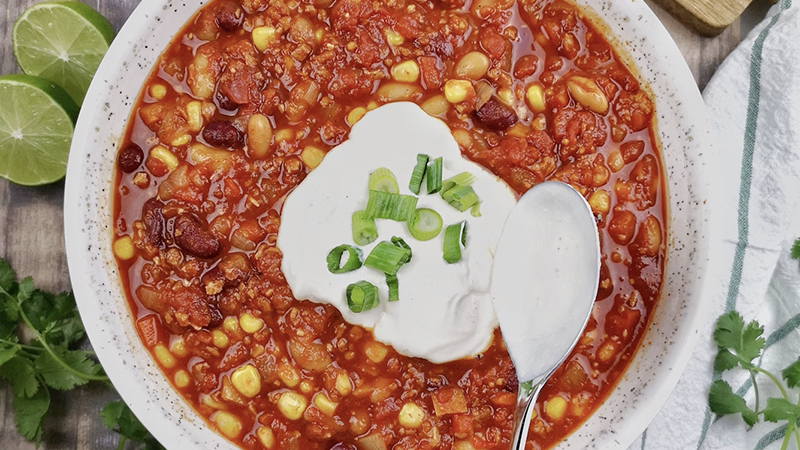 A steaming bowl of chili garnished with sour cream, shredded cheese, and green onions, perfect for a cozy fall evening.