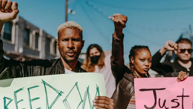A diverse group of activists outdoors, holding signs and raising fists, advocating for freedom and justice.