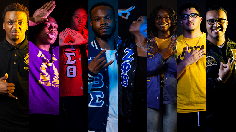 A vibrant group of Divine 9 members showcasing their Greek pride with colorful lighting and fraternity/sorority hand gestures.