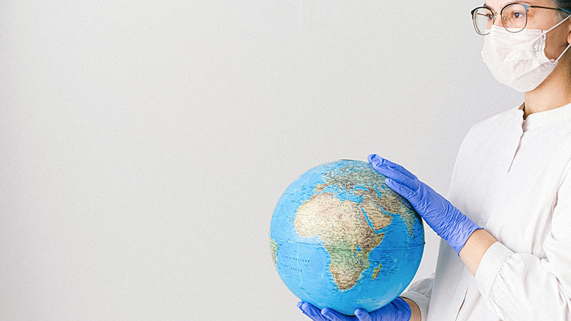 A healthcare professional wearing a face mask and gloves holds a globe, symbolizing global health and the importance of universal healthcare systems.