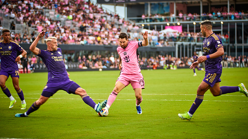 Lionel Messi dribbles past defenders in a pink Inter Miami jersey during a match against Orlando City SC.