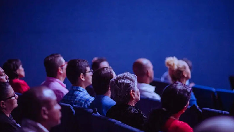 An attentive group of adults seated at an indoor conference, focusing on a presentation.